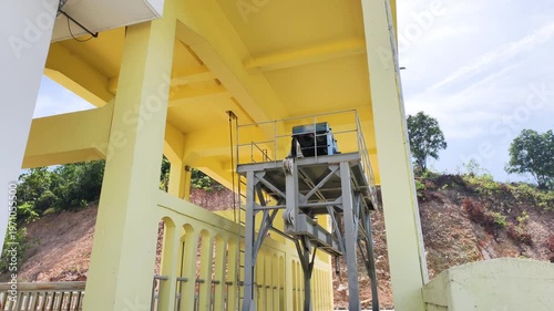 Side view shows engineering structure for sluice gates on a dam. A steel gantry crane stands on rails by a concrete wall. Functional engineering structure operates the sluice gates.