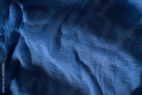 A piece of fabric lies on a surface as light catches its texture. The colors blend from purple to blue