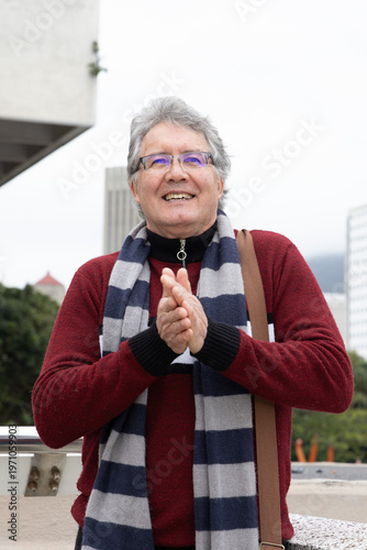 Bild auf Leinwand Senior man standing and clapping on outdoor terrace, wearing red sweater, stripe