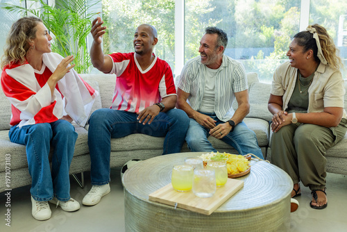 Raised hand starting conversation, four adults sitting on sofa gesturing, laughing, catching up