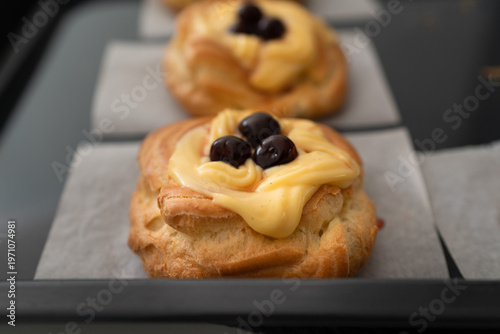 High-angle shot of traditional Italian Zeppole di San Giuseppe, handmade and fresh from the oven. The pastries are resting on a rustic black baking sheet lined with parchment paper, showcasing the gol
