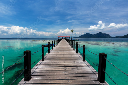 Fotografía Symmetrical view of a wooden pier stretching over clear turquoise waters and cor