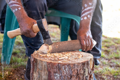 Indigenous man chopping wood with axe on tree stump making traditional wood carving