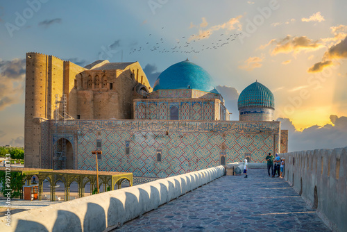 Turkistan, Kazakhstan - June 2, 2025: Golden hour view of the Mausoleum of Khoja Ahmed Yasawi (Hoca Ahmet Yesevi Türbesi) from the historical wall with flying birds and sun rays