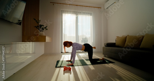 Fotografie A woman does glutes on a gym mat in a bright living room filled with sunlight