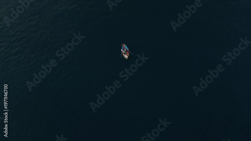 Fisherman in small boat paddles through calm waters at dawn, surrounded by the vast sea, showcasing the tranquility of early morning fishing off the coast of Italy