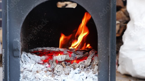 Fire burns steadily in a stove as embers glow brightly and ashes collect in the bottom for a warming experience
