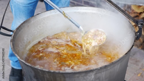 Cooking meat stew in a large pot over a fire outside during a chilly evening with friends and family gathering around