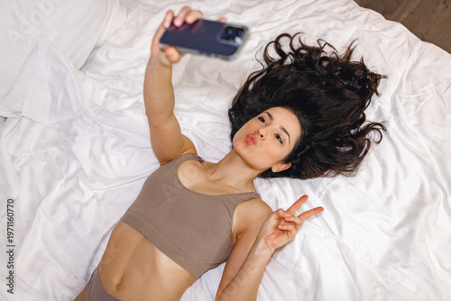Cropped photo of sexy young woman in underwear posing at bedroom while holding smartphone in her hands. Lifestyle concept