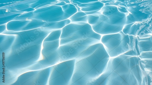 Bright sunlight glistens on crystal clear blue swimming pool water creating abstract shimmering patterns over the tiled bottom offering a refreshing calm mood