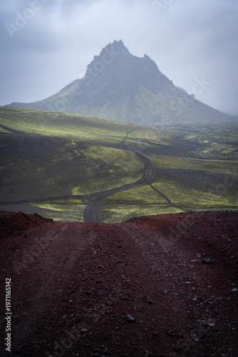 Vertical shot of solitary mountain with clouds above surrounded by green lichen fields, Iceland