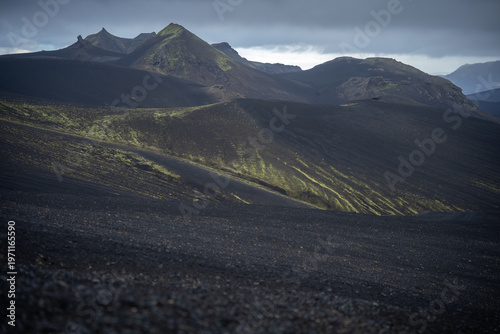 Volcanic landscape with mountains covered by black sand and green lichen, Iceland