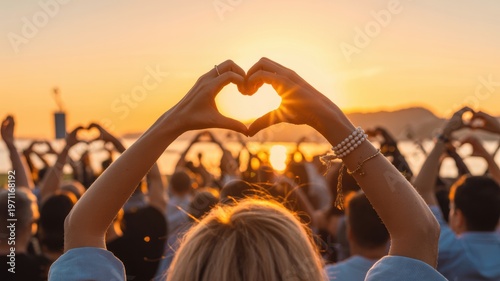 Hands create a heart shape framing the vibrant setting sun at a joyful outdoor gathering a large crowd participates in expressing love and unity under warm ligh