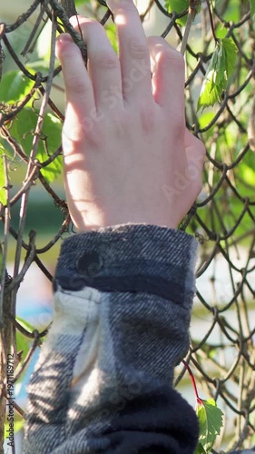 Close-up of a young man’s hand gripping a wire fence, symbolizing sadness and bullying at school. The shot conveys emotional tension, isolation, and struggle.