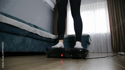 Low angle view of woman legs in black leggings white socks standing on black vibration platform for full body workout muscle toning home living room