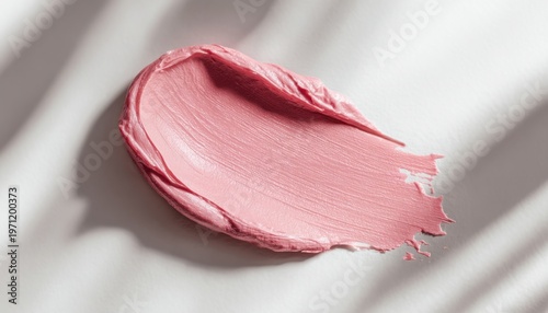 A smooth, glossy pink lip balm swatch on a light fabric surface with subtle texture and soft lighting