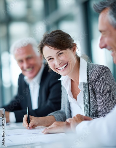 Confident businesswoman with short brunette hair smiling in a professional meeting setting, dressed in a tailored gray blazer and white blouse, engaging in conversation