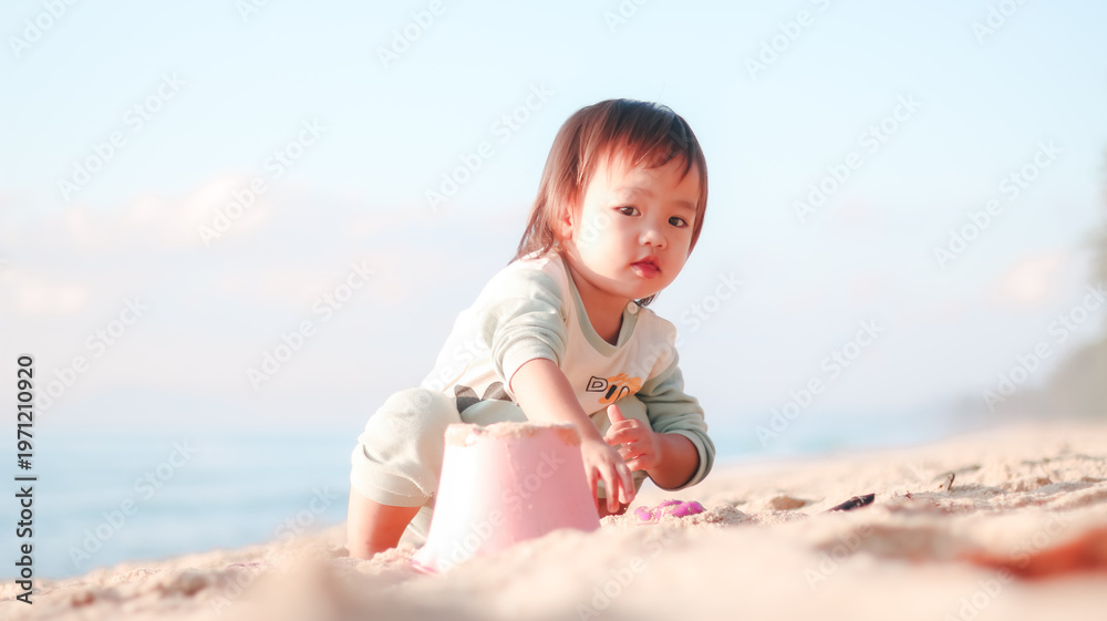 Fototapeta premium Beach play promoting early childhood development, sensory exploration, and creative learning. Asian toddler girl playing with sand toys by the sea, enjoying outdoor activity and natural discovery.