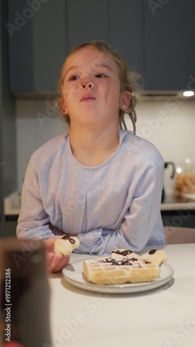 Young girl eating a delicious messy chocolate waffle in the kitchen