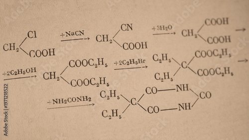 Foto A sequence of chemical reaction equations showing the organic synthesis of barbituric acid derivatives from chloroacetic acid printed on a page of old chemistry book