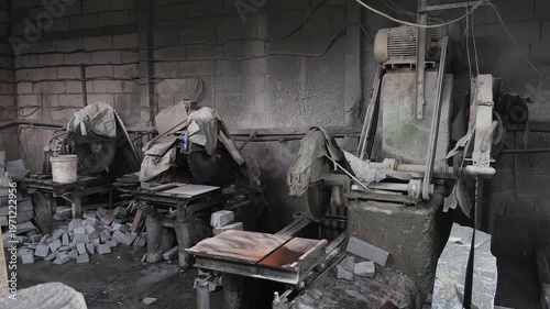 Inside a heavily dust-coated stone cutting workshop, large circular saws and masonry machinery sit idle. The thick layer of silica dust covering the equipment and floor