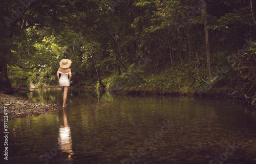 an elegant woman in a white dress and sun hat, together with serene reflective landscapes surrounded by lush green forest and soft natural light.