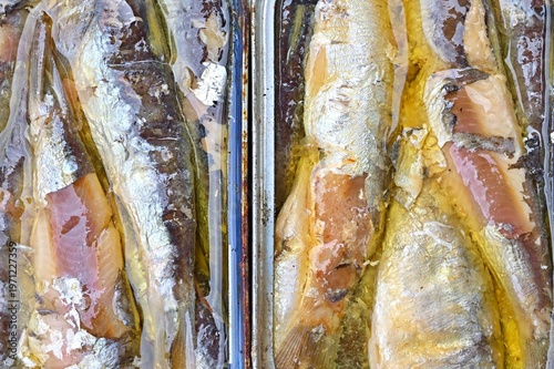 Two open metal cans packed tightly with oily, glistening preserved silver sardines.