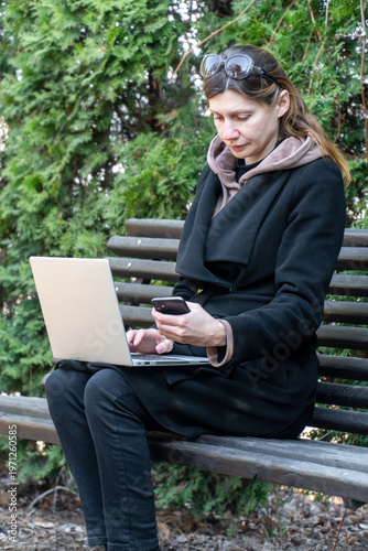 Woman using laptop and smartphone for two factor authentication in park