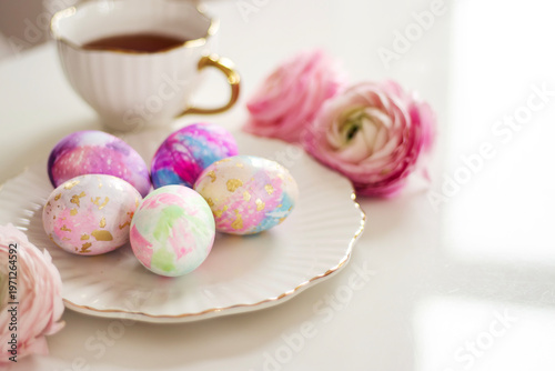 Wide composition of easter eggs with tea cup and flowers on light pastel background with large copy space.