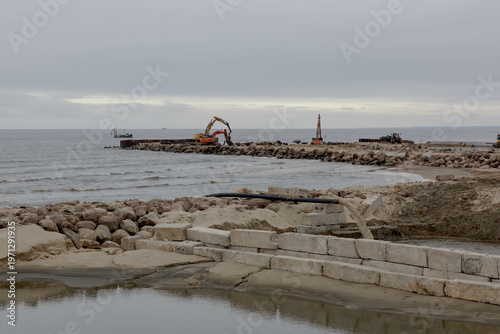 Фотография Construction of coastal breakwater with excavator and rocks on seashore