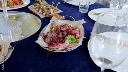 Gourmet grilled meats and charcuterie elegantly displayed on blue linen, accompanied by gleaming wine glasses, embodying refined culinary sophistication