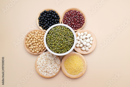 Top view of seven types of whole grains and legumes arranged in wooden bowls on a beige background