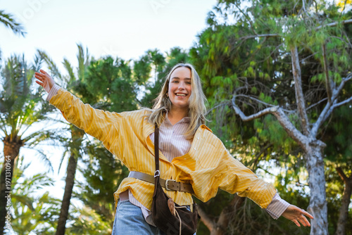 Travel blogger posing by historic bridge and palm trees on sunny day, solo female travel and city tourism concept, lifestyle content creator exploring destination in casual style.