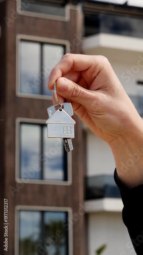 Man holding keys with house-shaped keychain in front of new apartment, real estate investment.