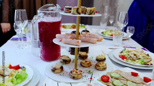 Sophisticated event catering display featuring gourmet appetizers, stuffed mushrooms, rolled ham, vegetable skewers on pristine white linen