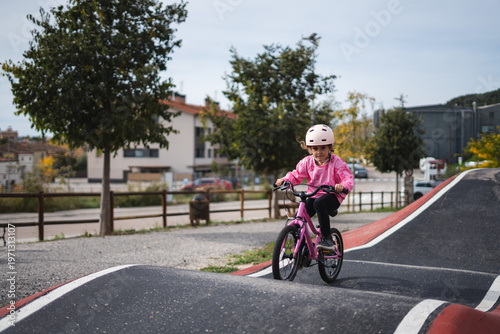A young girl riding a pink bicycle on a paved bike path in a suburban neighborhood
