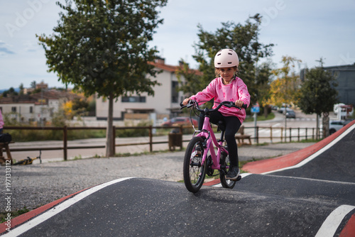 A young girl riding a pink bicycle on a paved bike path in a suburban neighborhood