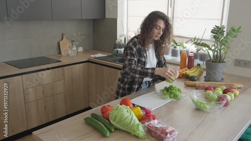 Woman Tearing Fresh Green Lettuce Leaves Into Bowl In Modern Kitchen