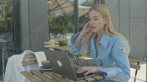 Concentrated Woman Working On Laptop At Outdoor Cafe Table In Sunny City