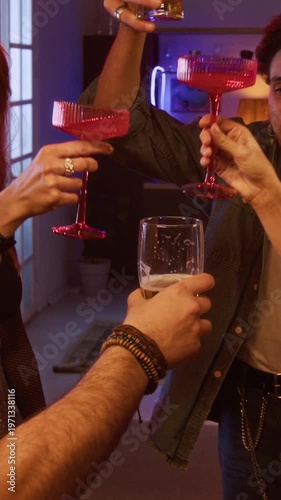Vertical shot of multiethnic group of young adults cheering with drinks while enjoying house party with DJ beats