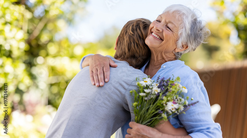 Elderly woman hugging her adult child and holding bouquet of daisies. Happy mother receiving flowers from offspring on Mother´s day. Family member greeting with affection in garden.