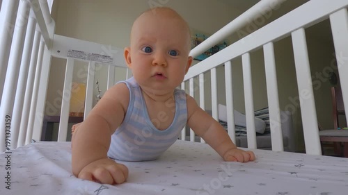 Cute 6 months old baby boy lying on his stomach in a cozy crib at home. Peaceful everyday moment of early childhood, safety and care. Infant development, parenting and baby comfort concept. Slowmotion