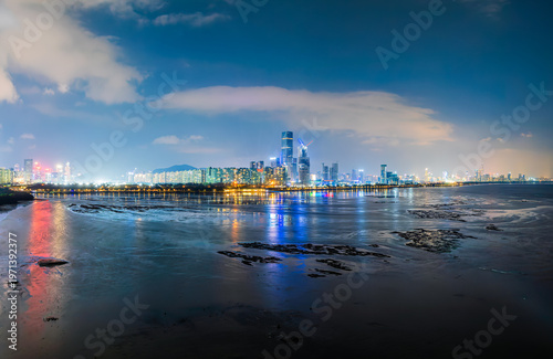 Night view of modern city skyline across the bay with coastal mudflats at twilight in Shenzhen, China.