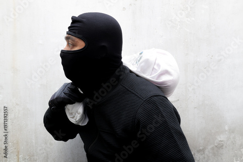 Photos Man in black balaclava holds white sack