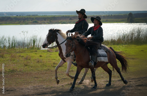 Cowboys riding horses along a scenic riverbank landscape