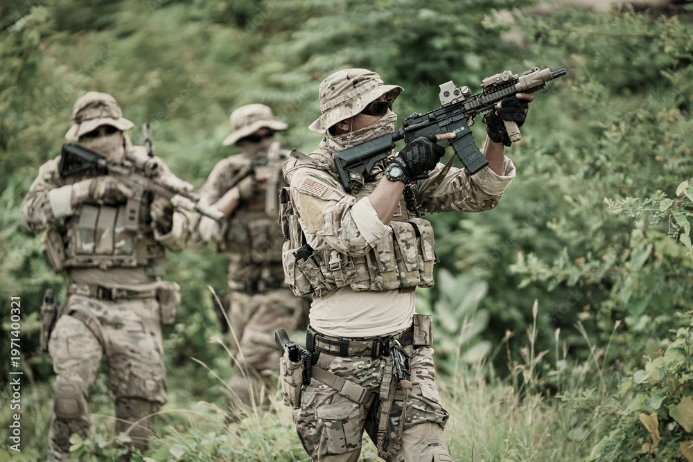 Obraz premium Military personnel in tactical gear advancing through dense vegetation