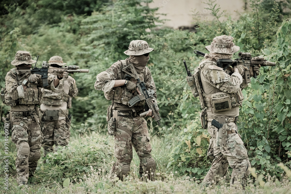 Fototapeta premium Special forces soldiers in camouflage gear advancing through dense foliage with rifles