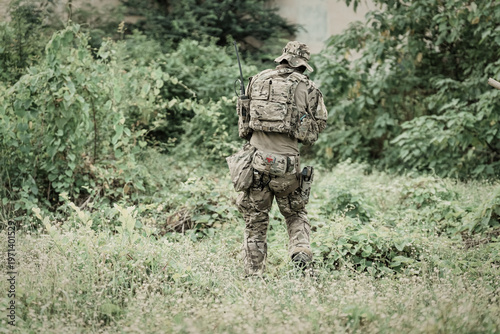 Bild auf Leinwand Soldier in camouflage gear walking through dense green foliage and grass