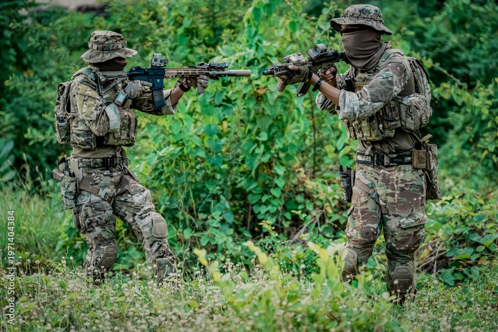 Fototapeta premium Two soldiers in camouflage gear aiming rifles in a dense green forest setting