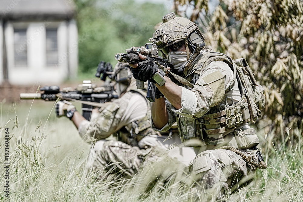 Fototapeta premium Special forces soldiers in camouflage gear aiming rifles in a grassy field